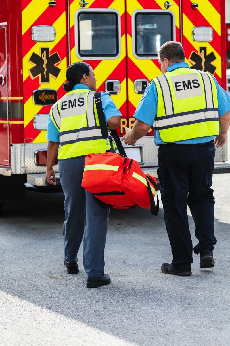 Two EMS medics in reflective vests walking toward the back of their ambulance