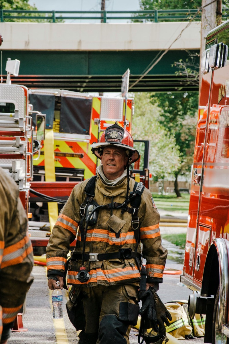 A firefighter in a red helmet and turnout gear walking between fire engines