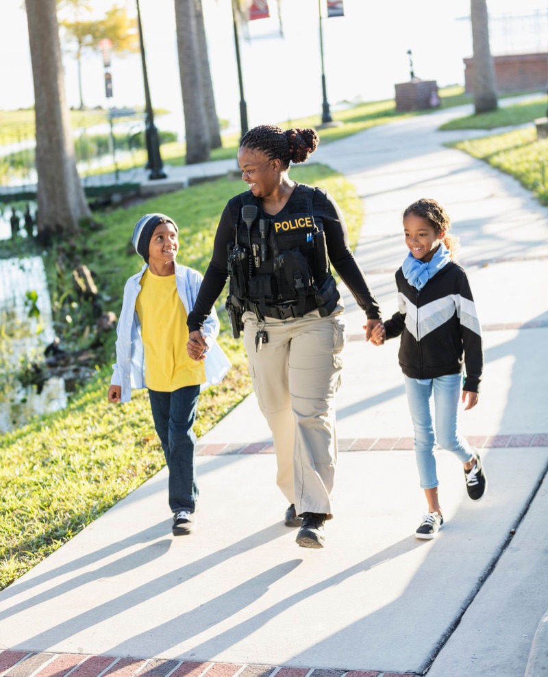 A police officer walking hand in hand with two children along a path lined with palm trees