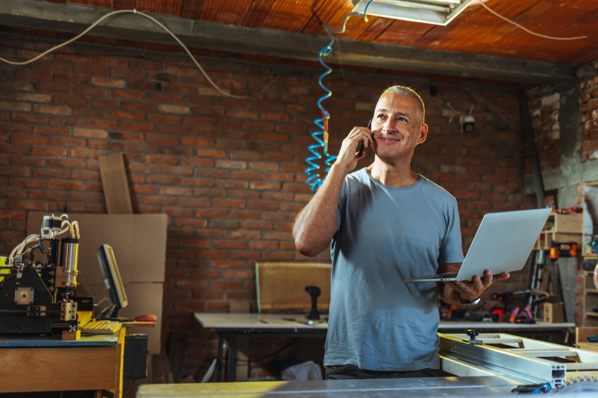 A business owner on the phone with a laptop in his workshop