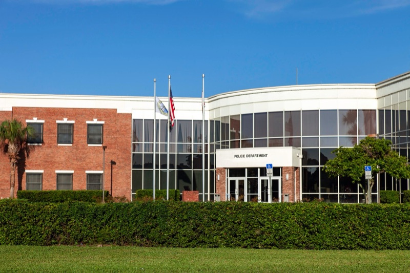 A police department building with flags and a palm tree out front